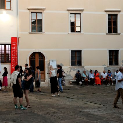 Na vhodu v križni hodnik zastava - obeležitev pokrovitelja Luka Koper - sklad Živeti s pristani&scaron;čem.